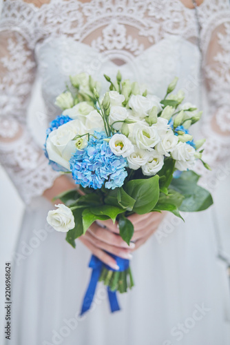 Hands of a bride in a white lace dress holding a wedding bouquet of roses, front view