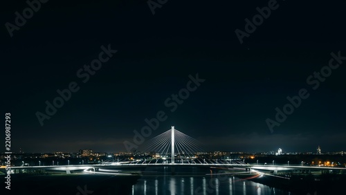 Modern illuminated cable stayed bridge spanning calm waters at night with city lights in background