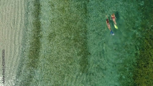 Aerial top-down view of two young women swimming and snorkeling with fins in the transparent turquoise water of the Pacific Ocean near a sandy beach on Coiba Island, Panama - stock video