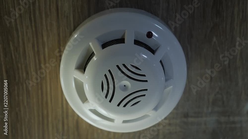 Smoke detector alarm system activation on wooden ceiling with warning red light flashing.