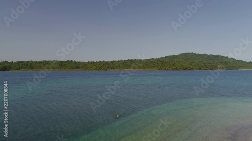Drone's view of a lush green island with a beautiful beach as two unrecognizable people are swimming in the calm, turquoise waters of Coiba Island National Park in Panama on a sunny day - stock video