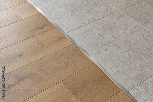 Oak wood flooring and gray stone tiles joined by a metal transition strip