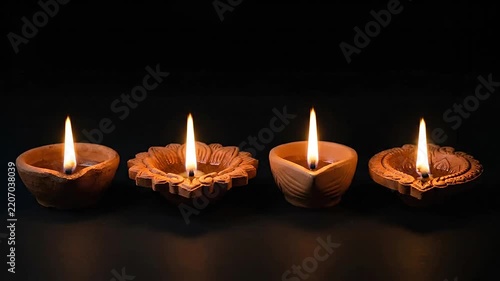 Four burning clay oil lamps glowing in a row on dark background
