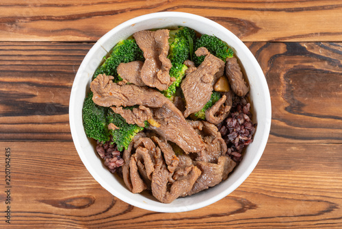 Beef grain rice bowl with broccoli in white disposable bowl on wooden table