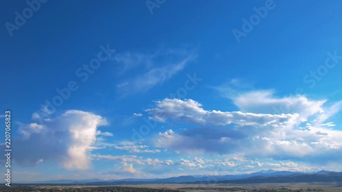 Panoramic aerial view of a vibrant blue sky filled with moving white cumulus clouds over distant hills.