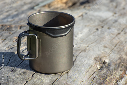 A titanium mug on an old wooden table. Camping cookware.