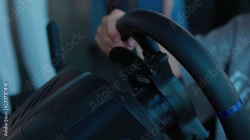 focused adult driving simulation setup in indoor gaming environment with steering wheel and pedals over the shoulder view in black and red plastic and metal materials.