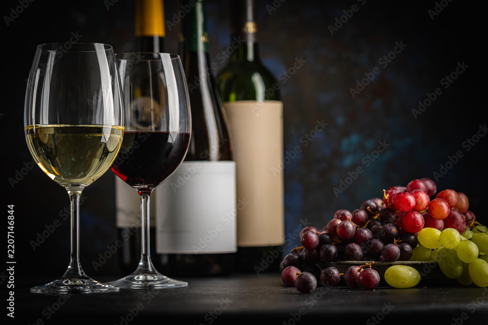 Obraz premium A dark, elegant still life of White and Red wine in a glass with wine bottles and fresh grapes in the background. Perfect for wine-themed compositions