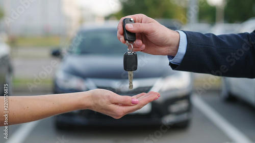 Car key handover during vehicle sale in outdoor parking lot with natural light