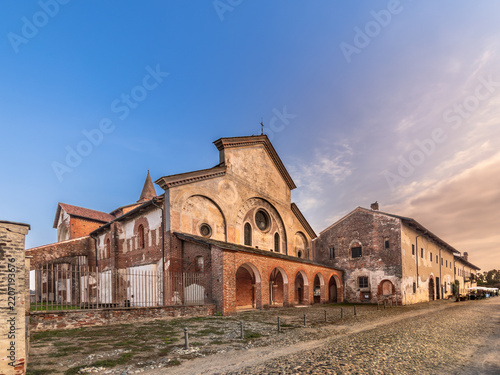 Revello, Piedmont, Italy - Santa Maria di Staffarda Abbey. Ancient 12th-century Cistercian monastery Romanesque-Gothic architecture with red brick facades, arches, and cobbled street, colorful sky.