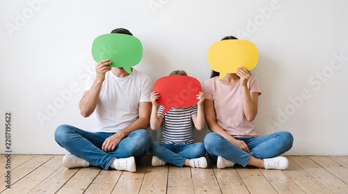 Family hiding behind colorful speech bubbles against a white wall playful communication concept