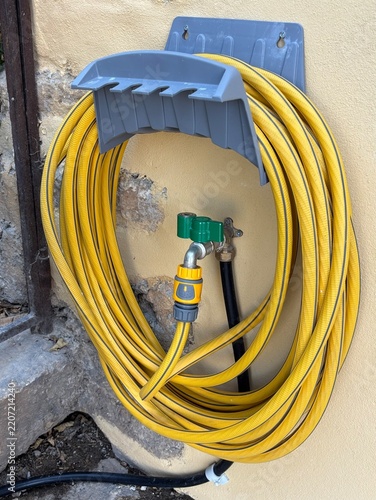 gelber Gartenschlauch auf blauer Halterung an einer Hauswand