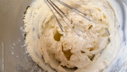 Fresh lemon-colored custard cream whipped with a whisk in a stainless steel bowl, showing its light and airy texture. The close-up baking scene represents homemade desserts, cake preparation