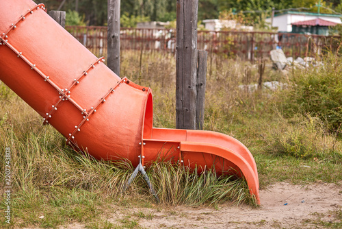 Fotografie Orange enclosed playground slide amid grass and rustic wooden posts