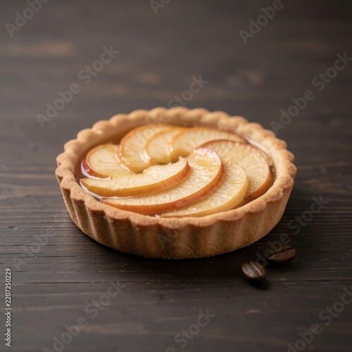 individual mini glazed apple tartlet with spiral apple slices on dark wooden table with scattered roasted coffee beans