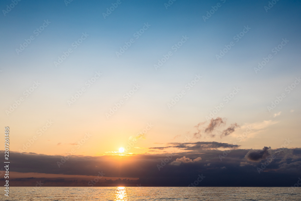 Fototapeta premium setting sun in dark sky over low clouds and sea