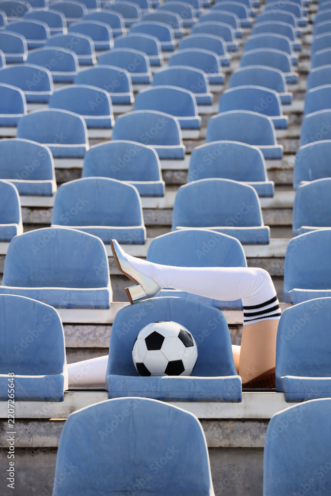 Obraz premium Sports fashion and femininity, woman legs in high heels and soccer socks with ball in empty stadium seats for creative advertising and lifestyle