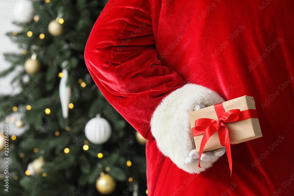Obraz premium Christmas surprise and holiday gift giving, Santa Claus hiding a present behind his back near a decorated tree for festive celebration and winter joy