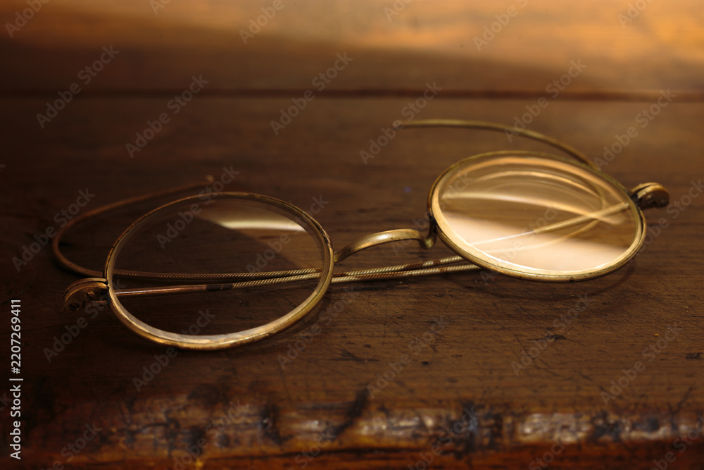 Naklejka premium Vintage spectacles resting on weathered wooden surface with warm ambient lighting. Intellectual themes