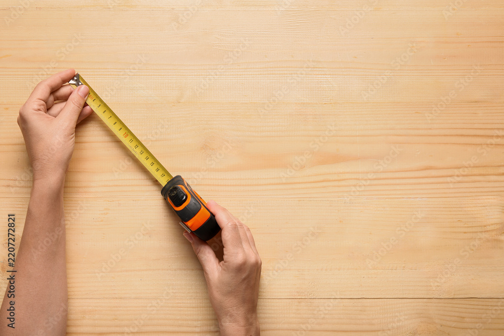 Fototapeta premium Home improvement and renovation planning, hands holding a measuring tape on a wooden table for construction project measurement and interior design