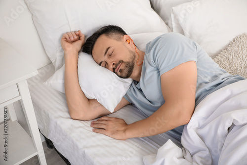 Sleep hygiene and relaxation, man sleeping peacefully in bed with earphones f...