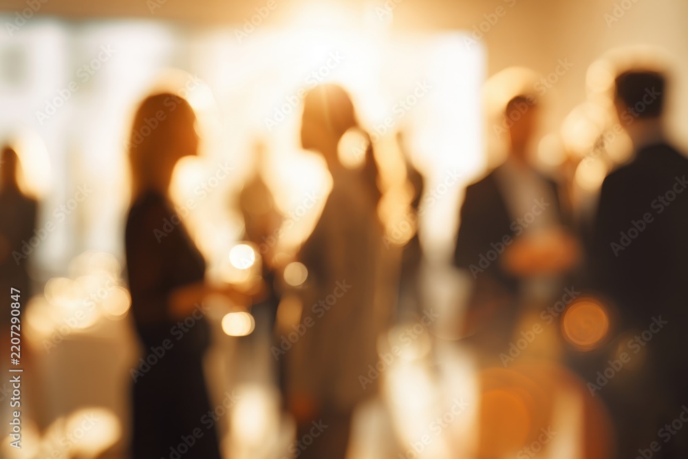 Fototapeta premium Blurred gathering of people socializing and engaging in conversations at a warm, softly lit networking event or casual business reception indoors