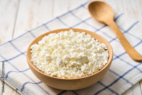 Fresh cottage cheese in a wooden bowl on a white table, selective focus.