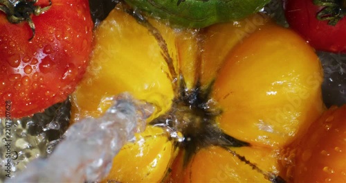 Raw tomatoes being splashed with water. Washing tomatoes before eating. Yellow, green and red tomato in a bowl of water. Healthy food. 