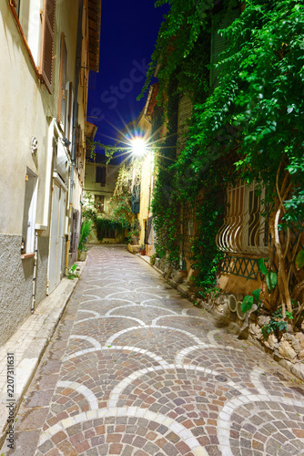 Cobblestone alley at night with fan-shaped paving pattern, glowing street lamp in Antibes Old Town, French Riviera, France