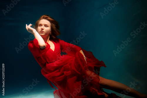 Calm female diver in flowing scarlet dress amidst bubbles and blue depths