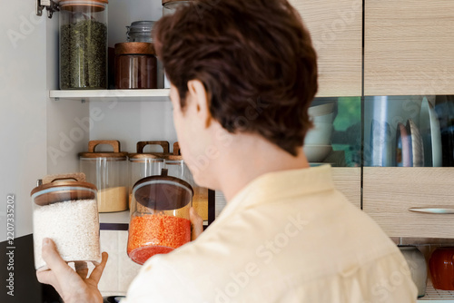 A man holding glass jars of rice and lentils for kitchen food storage. This selection of organic whole grains and cooking ingredients aids in pantry organization for daily cooking.