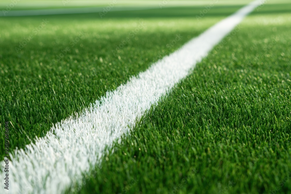 Fototapeta premium Close-up perspective of a vibrant green sports field featuring a crisp white boundary line extending into the distance on well-maintained artificial grass surfa