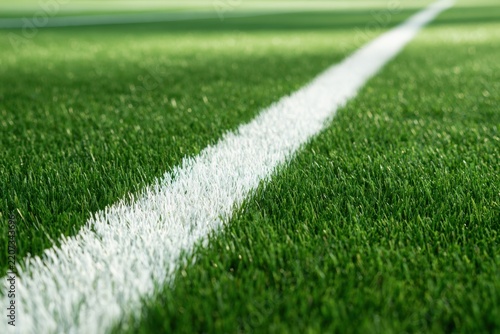 Close-up perspective of a vibrant green sports field featuring a crisp white boundary line extending into the distance on well-maintained artificial grass surfa