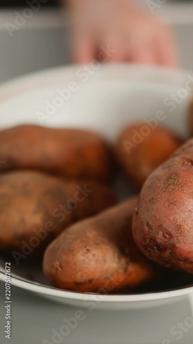Close up view of red potatoes in white bowl with occasional hand movement to adjust arrangement. Potatoes display natural skin texture and earthy tones against soft lighting emphasizing