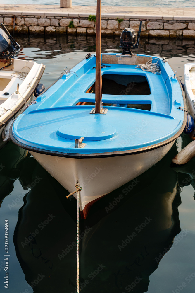 Fototapeta premium Boat anchored in calm waters near a stone pier surrounded by other boats at midday