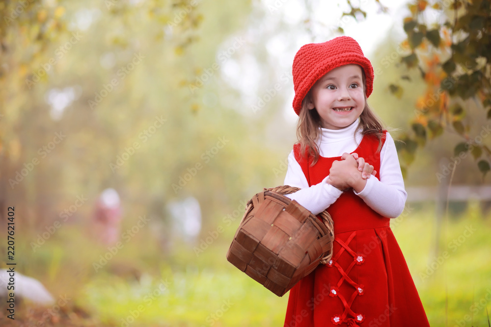 Obraz premium A little girl in a red hat and dresses is walking in the park. Cosplay for the fairytale hero 