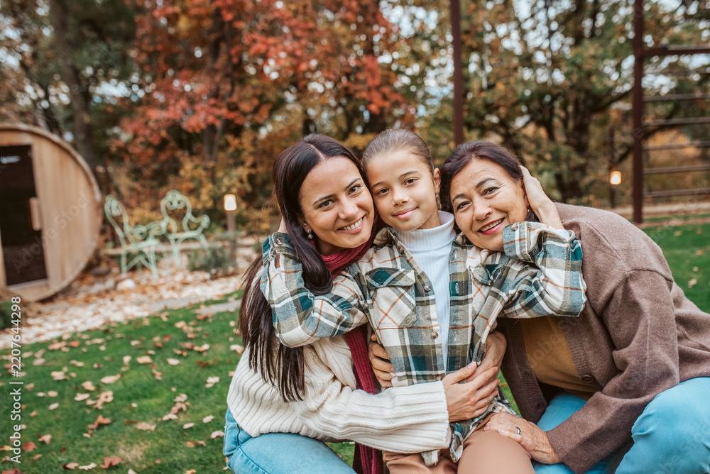 Obraz premium Mother, grandmother and granddaugter standing in autumn garden.