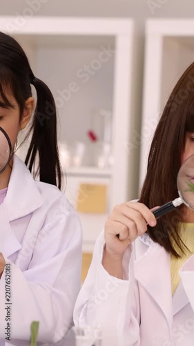Schoolgirls in Lab Coats Examining Plant Stem with Magnifying Glass