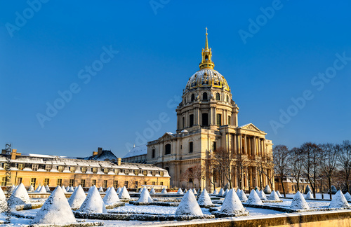 The gilded dome of Hotel des Invalides and snow covered topiary garden under a clear blue sky in winter in Paris, France.