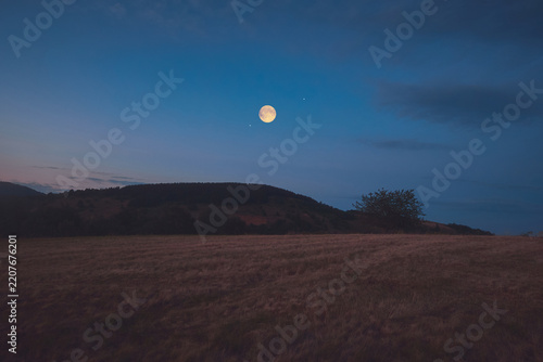 Full Moon, stars and planets above landscape silhouettes in blue hour time.
