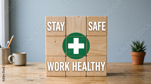 Nine light wooden blocks arranged in a three by three square grid on a wooden table displaying the text stay safe work healthy and a prominent green circle featuring a white medical cross symbol