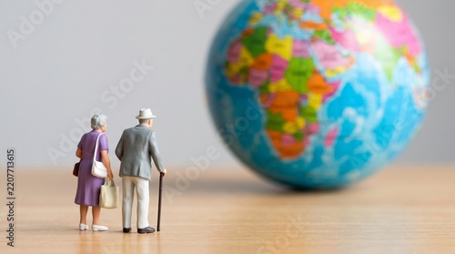 Miniature figurines of an elderly couple standing on a wooden surface looking at a globe with man woman stand