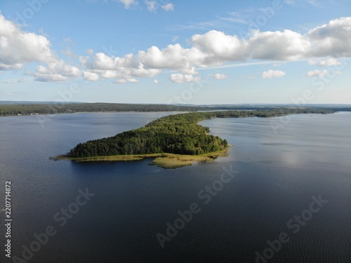 Wooded island in a broad lake beneath scattered summer clouds