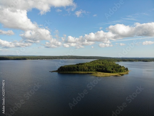Small forest island surrounded by calm blue lake water