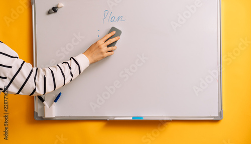 Hand wiping blue marks beneath Plan on a whiteboard with a gray eraser.