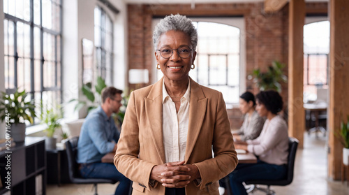 Portrait of confident senior African American businesswoman smiling at camera with team working behind