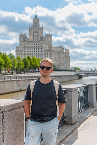 Photography Young man with a backpack on the embankment against a beautiful Stalinist high-r