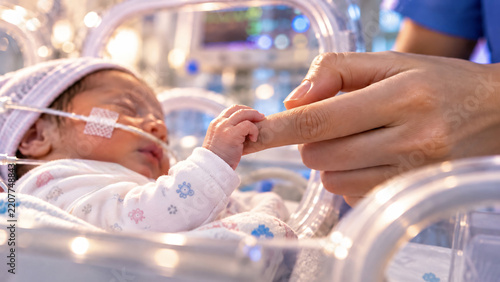 Premature newborn receiving specialized medical care in a neonatal intensive care unit while holding a parent's finger