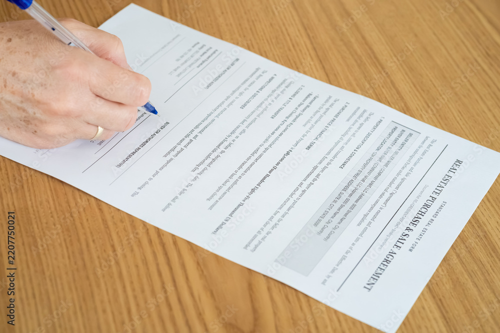 Obraz premium Real estate purchase and sale agreement contract with hand holding pen on wooden table close up 