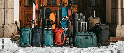 Various winter sports equipment and luggage are arranged neatly on snow in front of a rustic wooden door